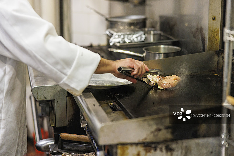 一个酋长，在餐厅的厨房里准备肉类，煎家禽。图片素材