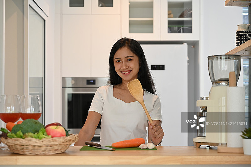 年轻的亚洲素食女性穿着休闲装，带着蔬菜，站在家里的厨房里，家庭生活和健康的生活方式理念。图片素材