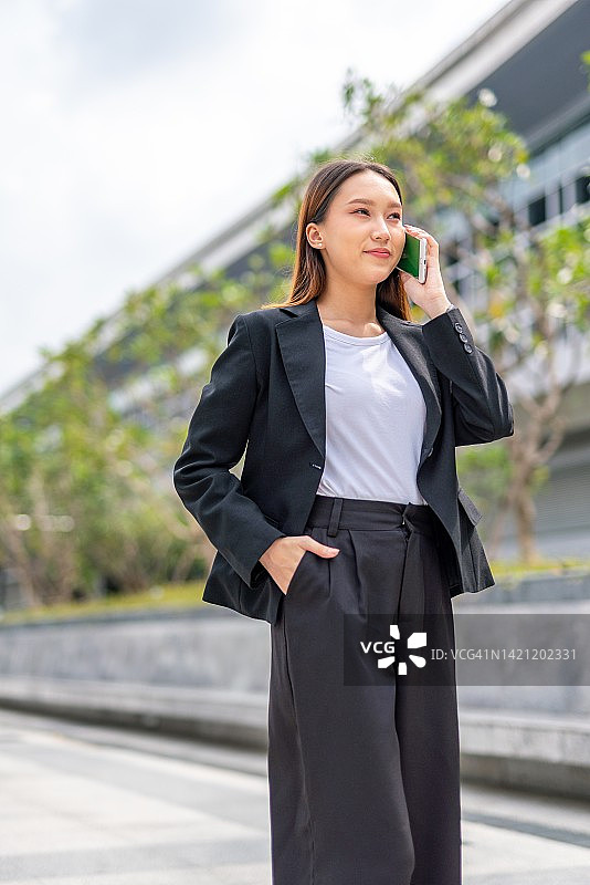 美丽年轻的亚洲女性办公室行政女士聊天电话与她的朋友在她的办公楼外图片素材