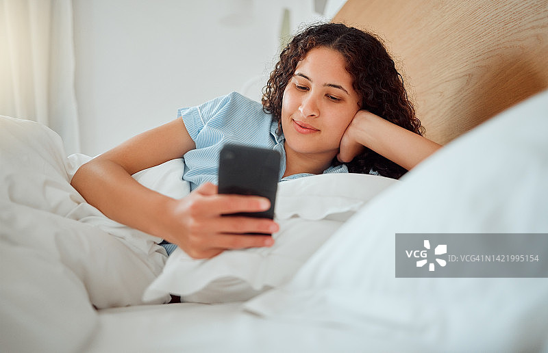 女人发短信，看短信，拿着手机看短信，早上醒着躺在床上。快乐，内容和微笑的女性玩游戏，浏览互联网或社交媒体图片素材