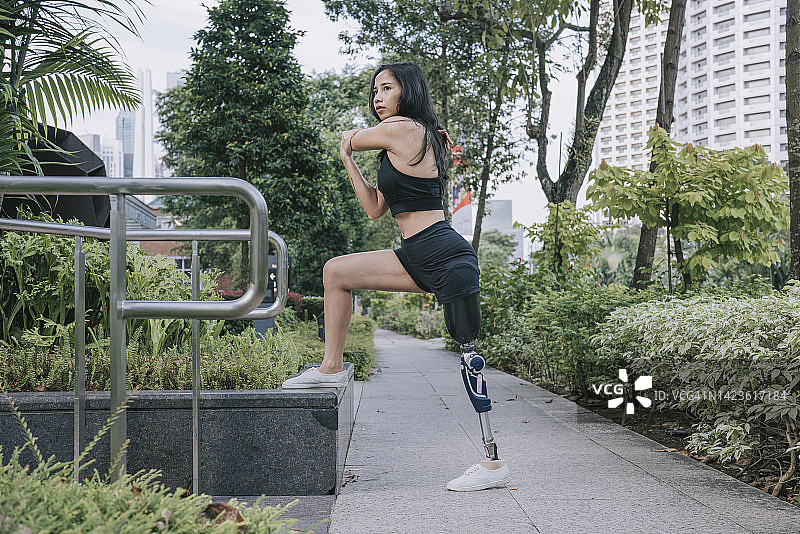 周末早上，亚洲残疾女运动员在城市步道进行人工腿热身运动图片素材