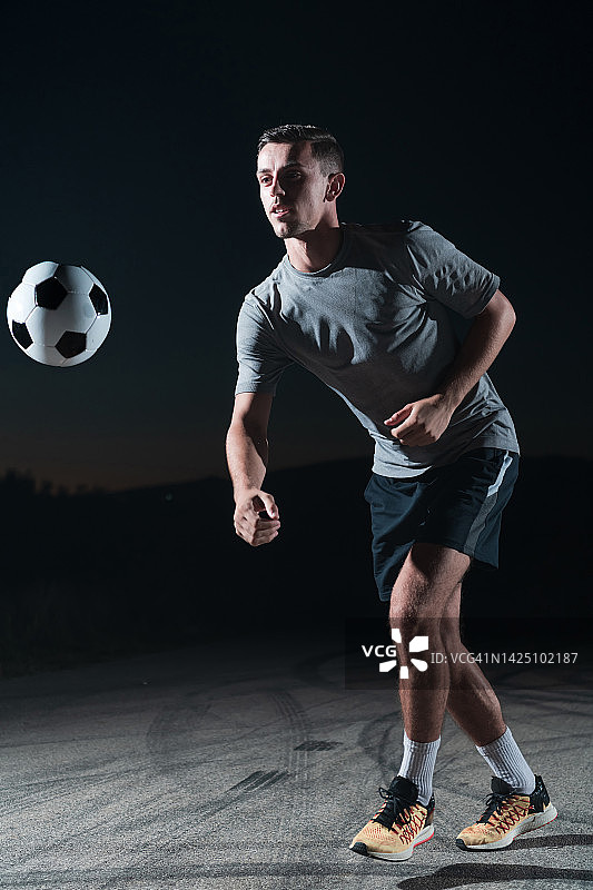 画像一个年轻英俊的足球运动员男子在街上玩足球。图片素材