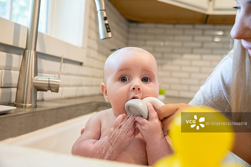 一位年轻的母亲正在家里的厨房水池里给襁褓中的儿子洗澡，并用毛巾把他裹起来图片素材