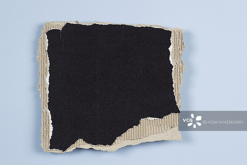 长方形一块黑色瓦楞纸板与撕裂的边缘在浅蓝色的背景。俯视图，复制空间图片素材