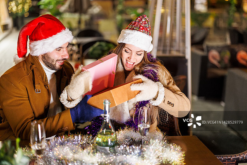 美丽时髦的夫妇戴着圣诞帽坐在餐厅里享受圣诞之夜。图片素材