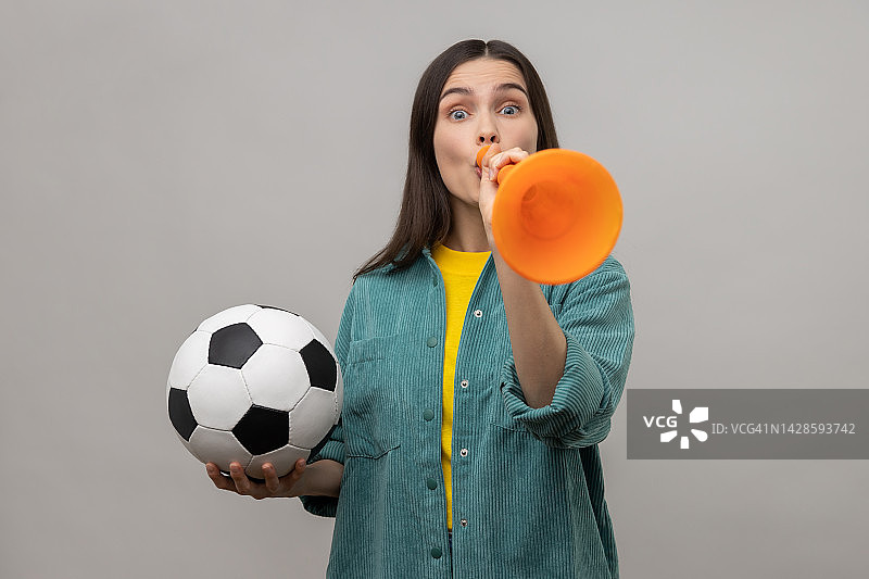 兴奋的女子拿着足球吹着喇叭，庆祝最喜欢的足球队的胜利。图片素材