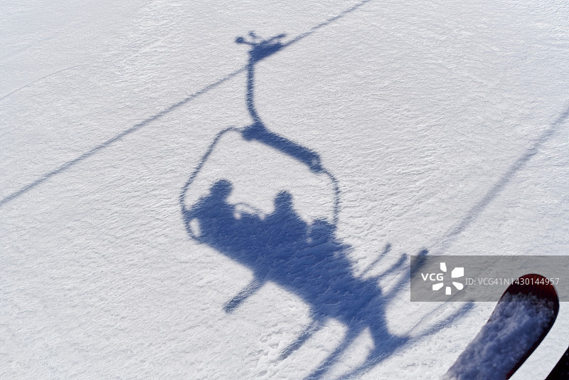 几个人带着他们的滑雪装备和缆车椅子上的缆绳的影子，下面是雪图片素材