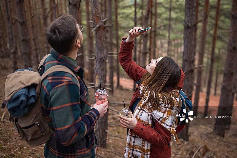 在阳光明媚的日子里，一名年轻女子和男友一起徒步旅行，用智能手机拍下了大自然的照片图片素材