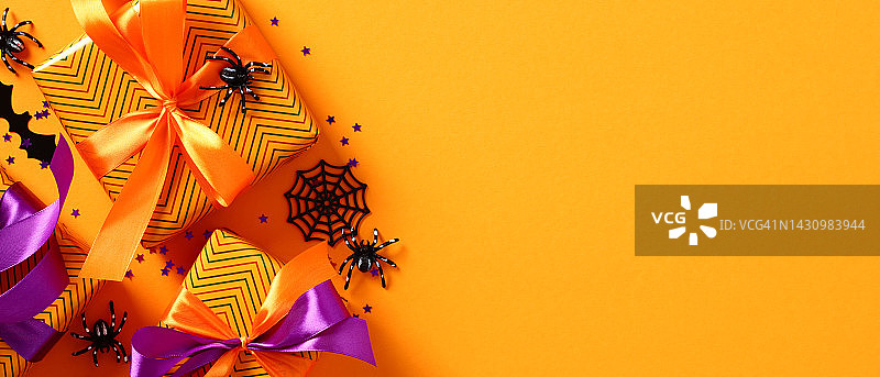 万圣节快乐节日横幅设计。平铺的礼品盒，蜘蛛，蝙蝠，橙色背景的五彩纸屑。带有复制空间的俯视图。图片素材