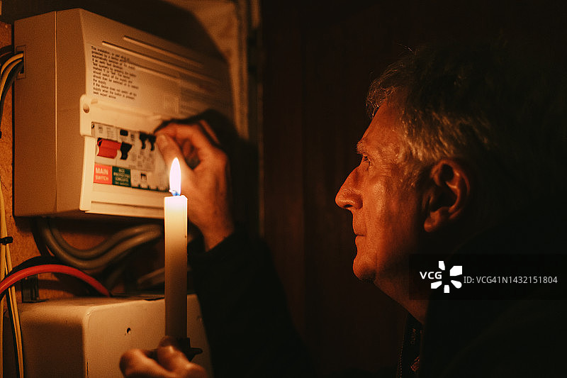 停电期间，老人在烛光下检查家用保险丝盒图片素材