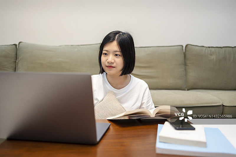 亚洲妇女在家里工作，笔记本电脑和手机在客厅图片素材