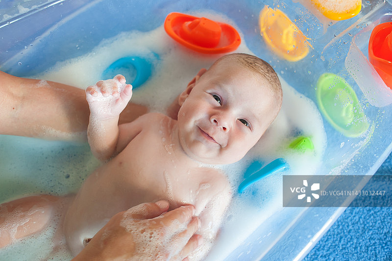 快乐微笑的宝宝沐浴在有泡沫泡沫的水中图片素材