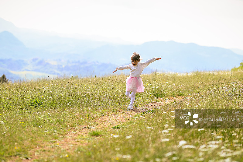 快乐的小女孩在草地上奔跑。3岁蹒跚学步的女孩张开双臂在草地上奔跑，小快乐的女孩。夏天有趣的户外活动。图片素材