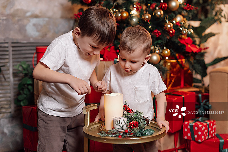 快乐的孩子们穿着轻薄的衣服，装饰着圣诞的装饰品。新年。圣诞树。礼物。蜡烛。红色和绿色图片素材