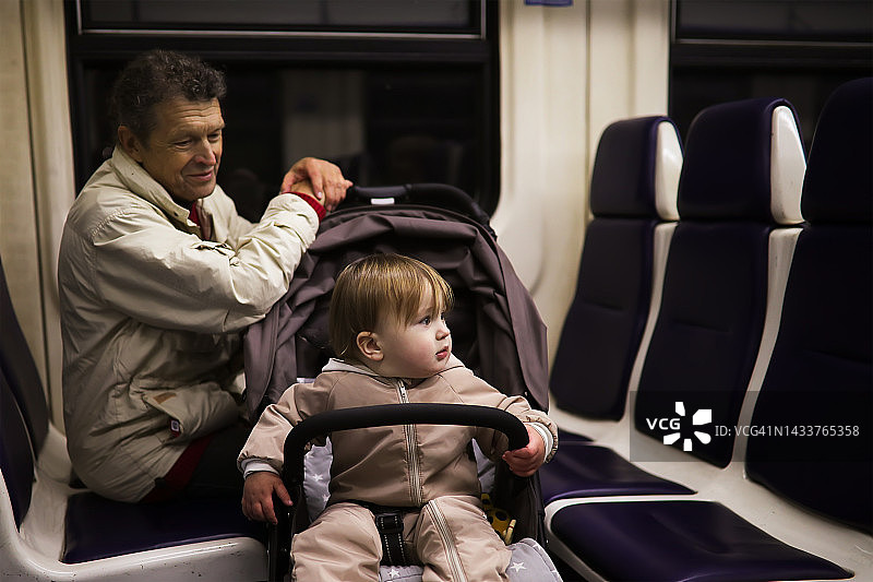 老人坐在婴儿车孩子蹒跚学步的火车。爸爸和他的儿子孙子旅行。图片素材