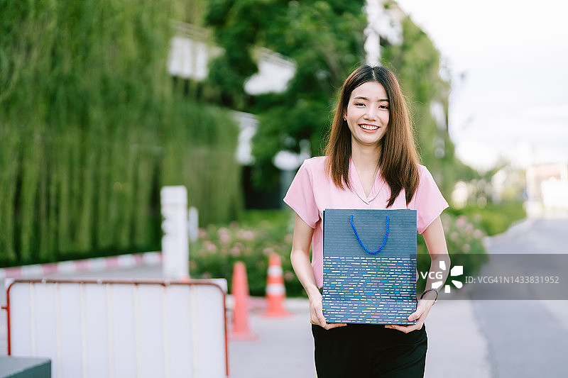 年轻的亚洲妇女拿着购物袋在商场前看着镜头微笑着快乐的脸。图片素材
