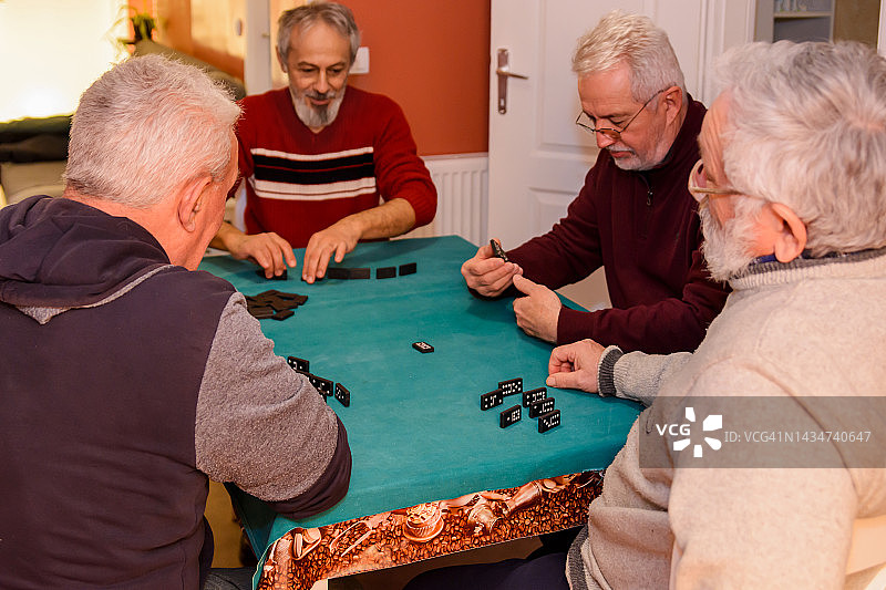 一群退休人员在家里玩多米诺骨牌，享受着他们的时光。图片素材