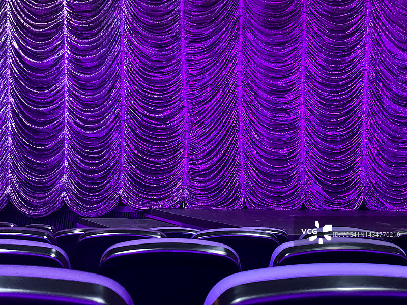 昏暗的灯光豪华紫色剧院窗帘与几排座位的观点。艺术、戏剧、演艺业、娱乐和电影概念图片素材