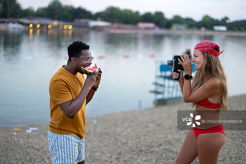 一名年轻的非洲男子和他的女性朋友在海滩上享受时光并拍照。图片素材
