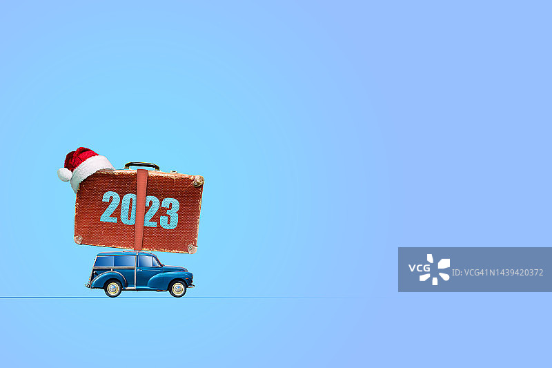 车顶上有个行李箱的车。2023年,数字。圣诞老人的帽子。在蓝色背景上。副本的空间。新年贺卡。节日图片素材