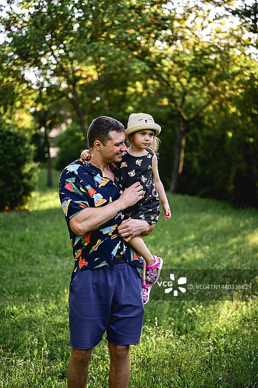 年轻的父亲带着他的女儿在夏天夕阳下的草地上的乡村画像。一家人在绿色的草地上远足。图片素材