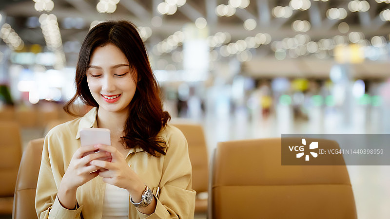 亚洲妇女在机场等待离开假期假期。亚洲女乘客坐在候机大厅用手机等机图片素材