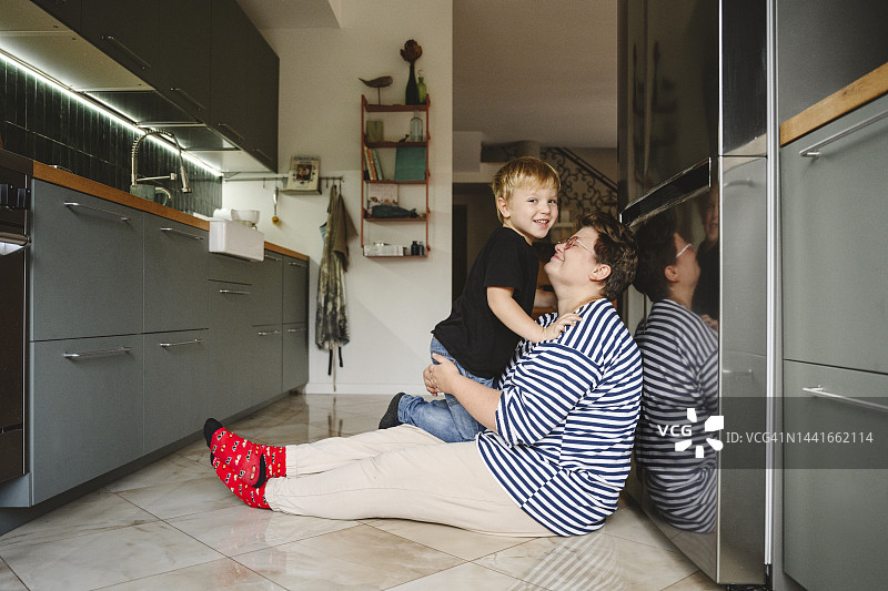 快乐的儿子和妈妈坐在厨房的地板上图片素材