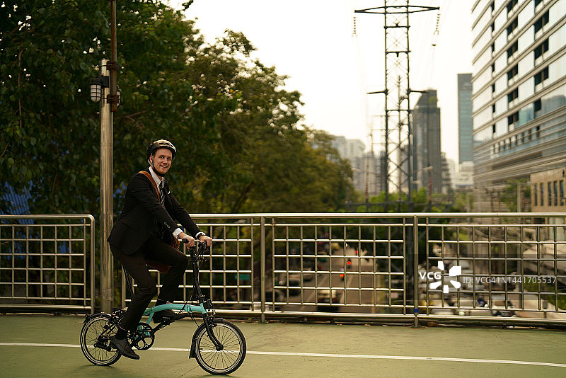快乐的商人骑着自行车在城市街道上旅行图片素材