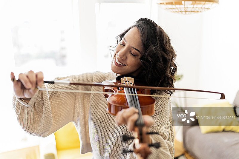 年轻女子面带微笑在家里拉小提琴图片素材