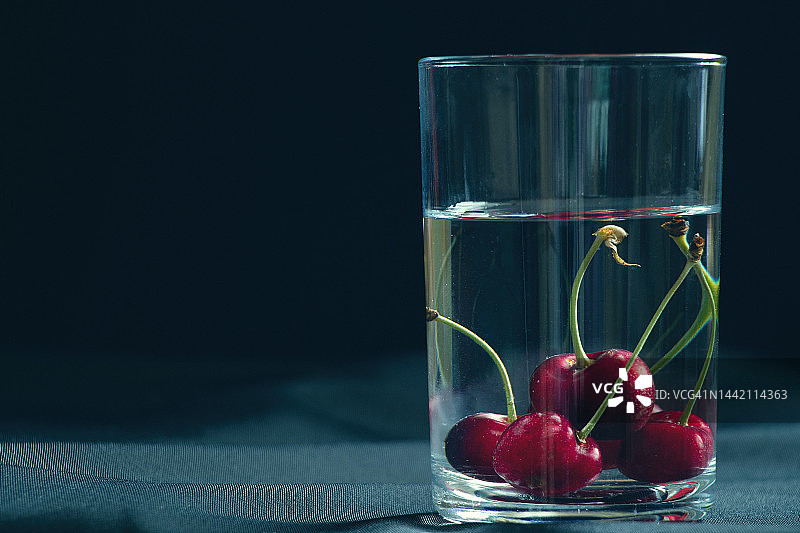 樱桃在一杯水上黑色的背景在桌上，水果的背景图片素材