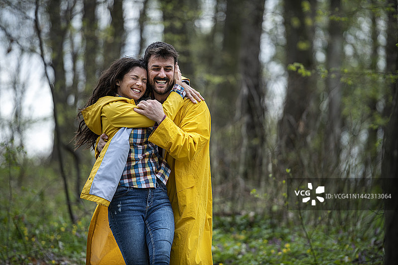 一对穿着雨衣的幸福夫妇在森林里愉快地拥抱和散步图片素材