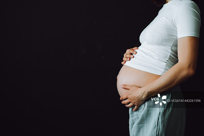 孕妇的保健和保护。孕妇腹部的中部在白色内衣和t恤上的黑色视图图片素材