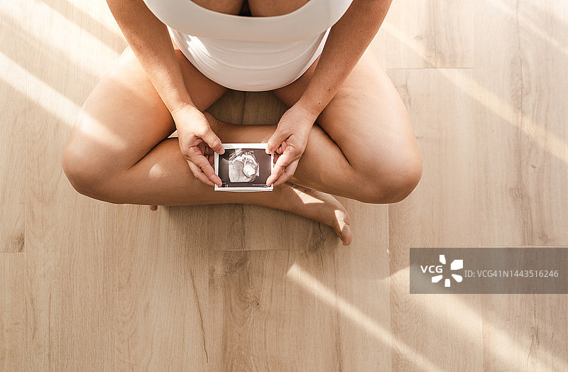 航拍的孕妇坐在地上，手里拿着婴儿超声波。图片素材