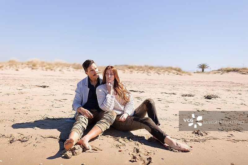 一对情侣坐在沙滩上看海，享受冬日阳光明媚的日子图片素材