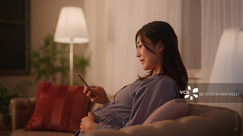 孕妇坐在沙发上放松，在家里的客厅里使用手机图片素材