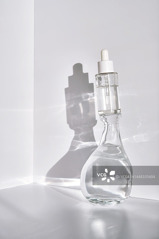 一个透明的装有血清的瓶子和一个装有水的容器，在阳光下的白色背景下有阴影。图片素材
