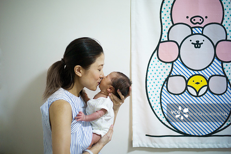 年轻的亚洲母亲在沙发上亲吻怀里的满月婴儿图片素材