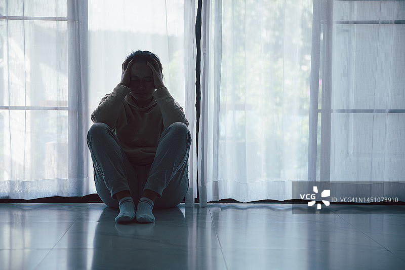 精神分裂症具有孤独和悲伤的心理健康抑郁症概念。抑郁的女人坐在地板上，在黑暗的房间里感到痛苦。女人沮丧、害怕、不快乐。图片素材
