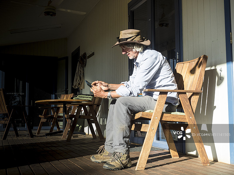 戴着帽子的中年男子在昆士兰州内陆的一个阳台上看着平板电脑。图片素材