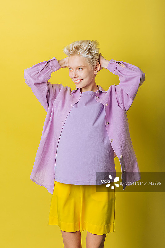 积极的年轻金发女子短发紫色衣服在黄色背景工作室拍摄图片素材