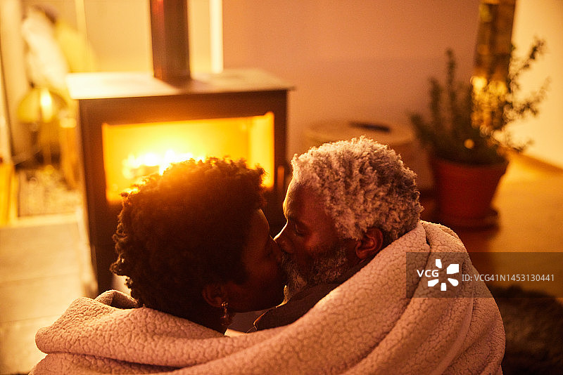 热恋的情侣裹在毯子里，在壁炉旁亲吻图片素材