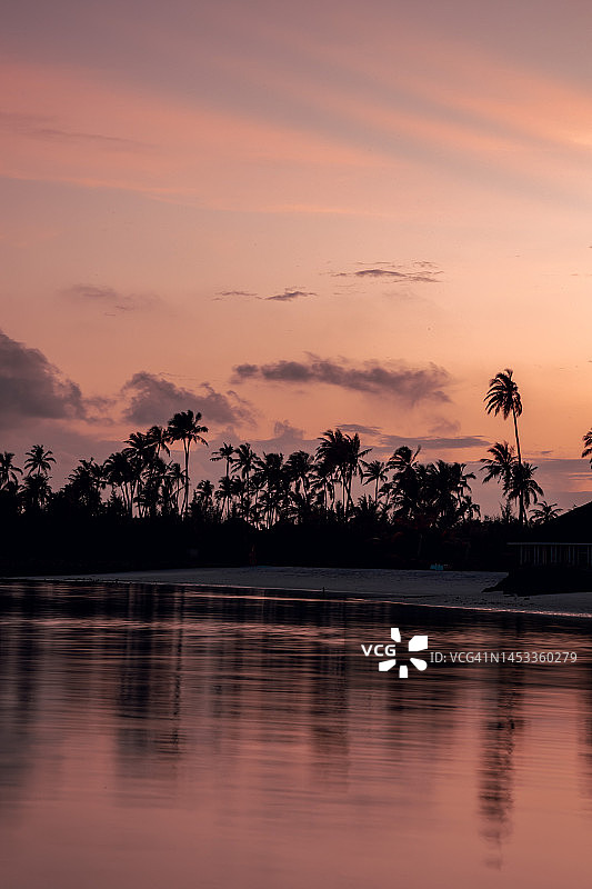 五彩缤纷的日落在海滩与水反射热带马尔代夫岛的棕榈树图片素材