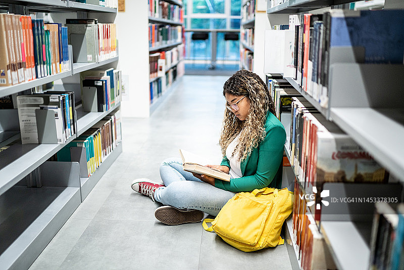 年轻的女学生坐在大学图书馆的地上图片素材