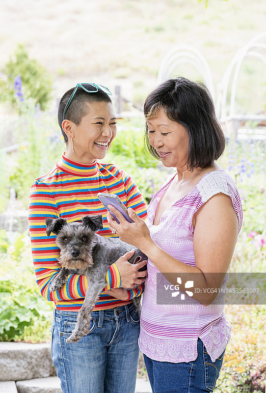 母亲带着成年的女儿和他们的狗站在后院的花园里图片素材