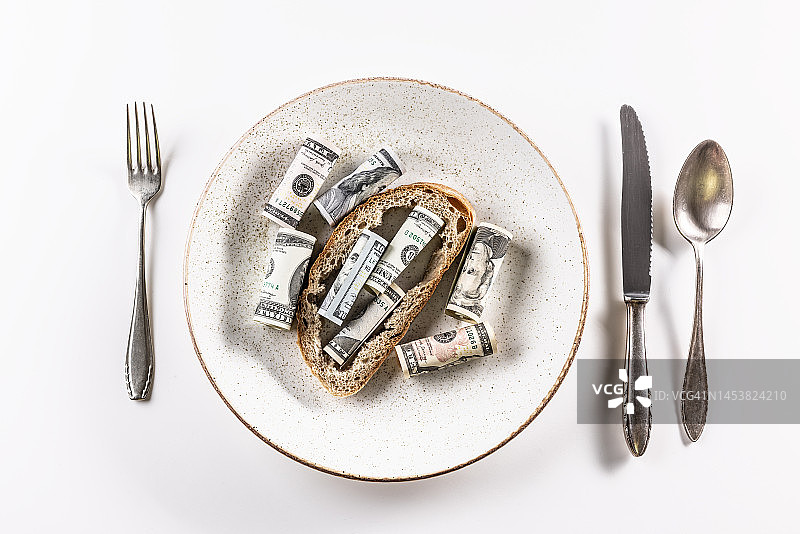 面包皮上放满了美钞，盘子里有白色背景的餐具。图片素材