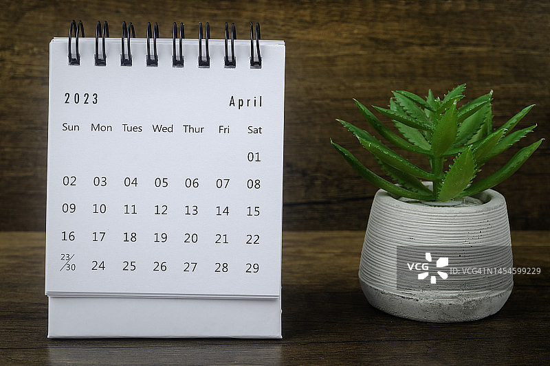 日历桌2023:4月是组织者计划和截止日期的月份，在木质桌子背景上放置室内植物。图片素材