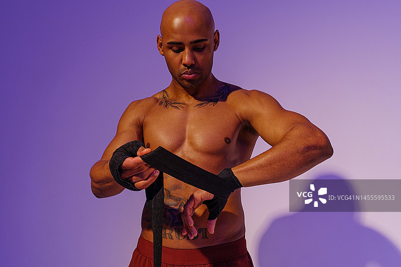 运动男子与裸露的躯干胶带他的手臂与绷带在工作室背景前战斗图片素材