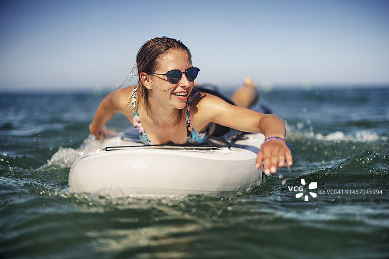 一个十几岁的女孩正在夏日的海边享受SUP冲浪板图片素材