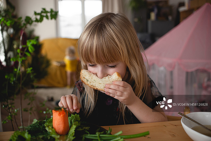 一个小女孩在家里的厨房里开心地吃着新鲜的香草和面包。儿童适当营养的概念。图片素材