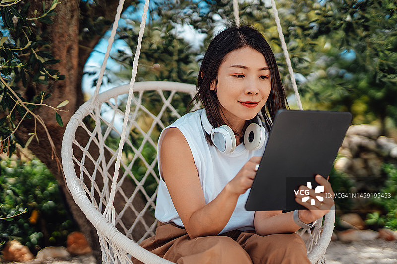 年轻的亚洲妇女工作与数字平板电脑在家里的花园放松图片素材